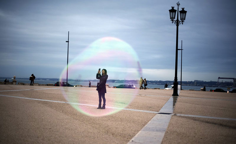 a-tourist-is-seen-through-a-soap-bubble-as-she-takes-a-picture-at-comercio-square-in-downtown-lisbon-on-november-18-2014